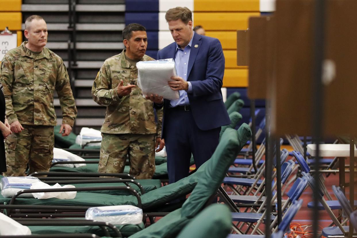 New Hampshire Gov. Chris Sununu, right, examines bedding packets as he tours a makeshift medical facility with N.H. Army National Guard Col. David Mikolaities, center, and N.H.A.N.G. Col. Erik Fessenden, left, at a gymnasium at Southern New Hampshire University in Manchester, N.H., Tuesday, March 24, 2020. The facility, and others across the state, will open when there is demand for patients impacted with COVID-19. For most people, the new coronavirus causes only mild or moderate symptoms. (AP Photo/Charles Krupa)