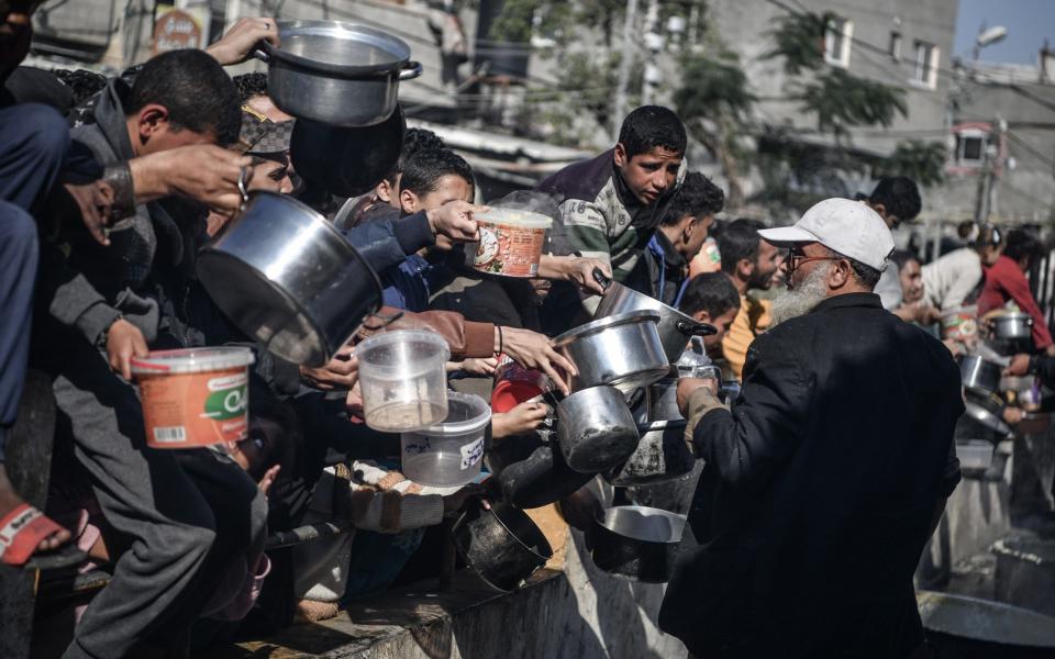 People, including children, wait in a long line to receive a small amount of food in the city of Rafah, southern Gaza Strip.