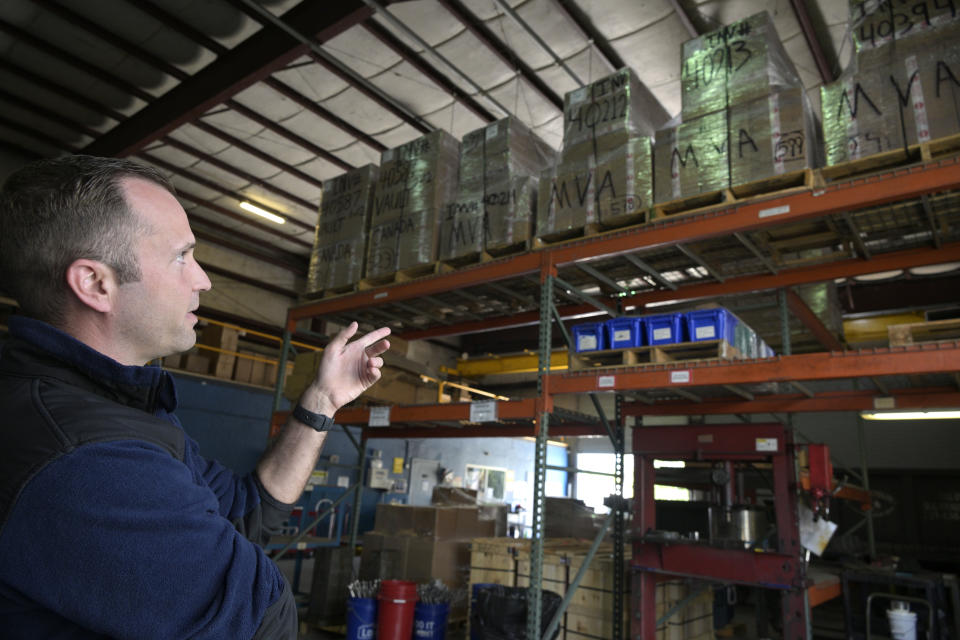 Adrian Kellgren points to pallets wrapped in plastic stacked on warehouse shelves.