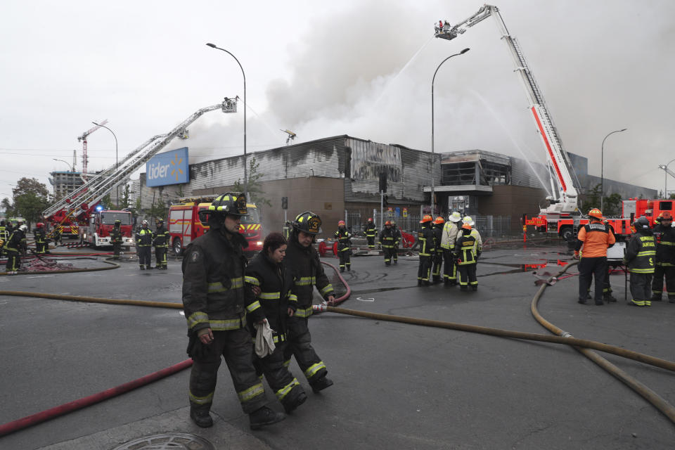 Firefighters spray water on a looted supermarket in Santiago, Chile, Sunday, Oct. 20, 2019. Chilean President Sebastián Piñera on Saturday announced the suspension of a subway fare hike that had prompted violent student protests, less than a day after he declared a state of emergency amid rioting and commuter chaos in the capital. (AP Photo/Esteban Felix)