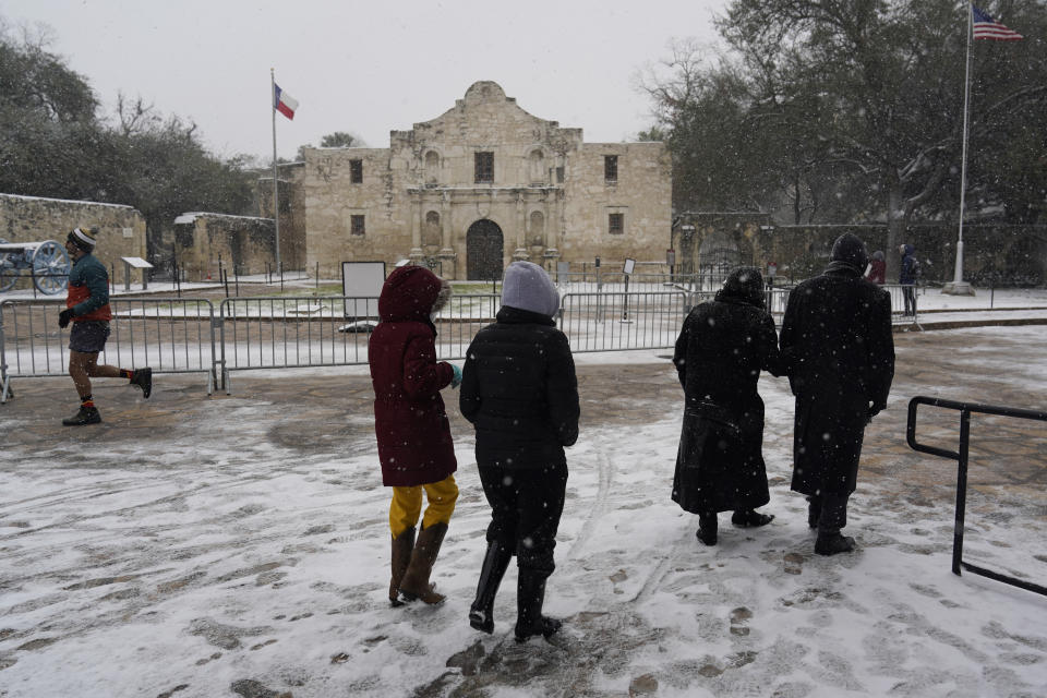 FILE - People walk through the snow as they pass the Alamo, Thursday, Feb. 18, 2021, in San Antonio, as ice and sub-freezing weather to wreak havoc on the state's power grid and utilities. According to three different reports released Monday, Jan. 10, 2021, the United States staggered through a steady onslaught of deadly billion-dollar climate disasters in an extra hot 2021, while the nation’s greenhouse gas emissions last year jumped 6% because of surges in coal and long-haul trucking, putting America further behind its 2030 climate change cutting goal. (AP Photo/Eric Gay, File)