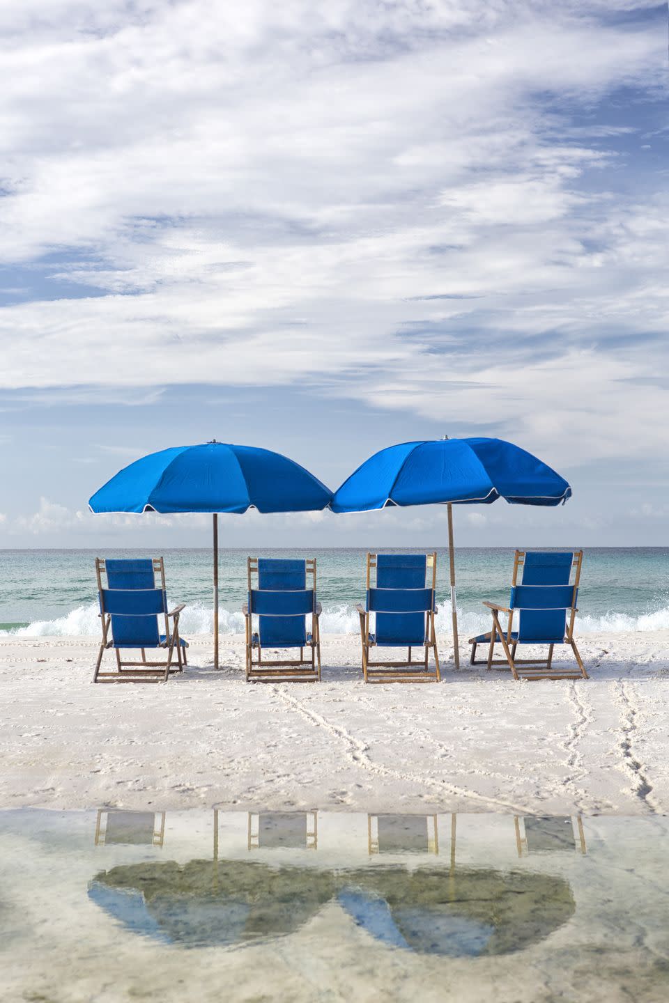 blue beach chairs and umbrella on white sand facing surf