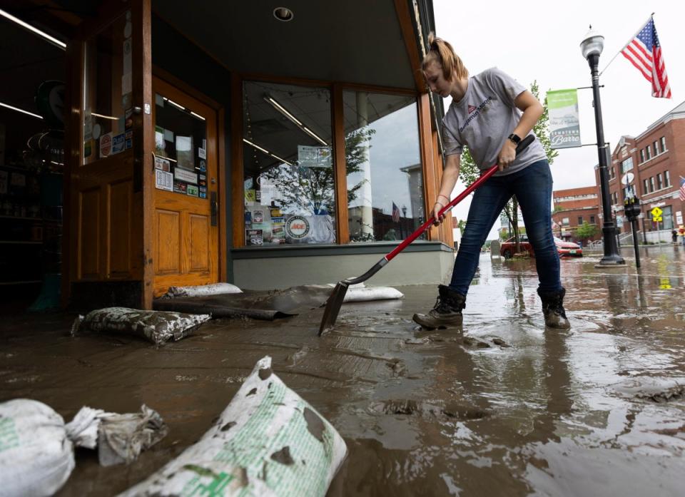 Zyta-Rose Blow, an employee at Nelson Ace Hardware, shovels mud and silt from the shop on Main Street in Barre, Vermont on Tuesday (EPA)