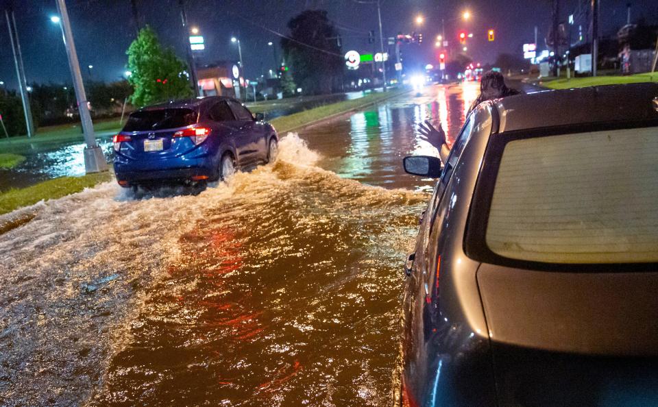 Lamont Pepp, right, waves to a passing motorist to slow down after Pepp's car stalled in high water in Slidell, Louisiana, late Friday, June 18, 2021, as a tropical disturbance neared the Louisiana shore.