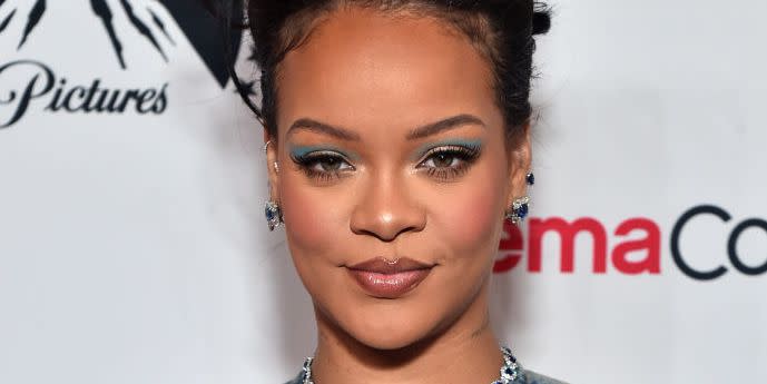 rihanna with her hair up and blue eye makeup poses on a carpet