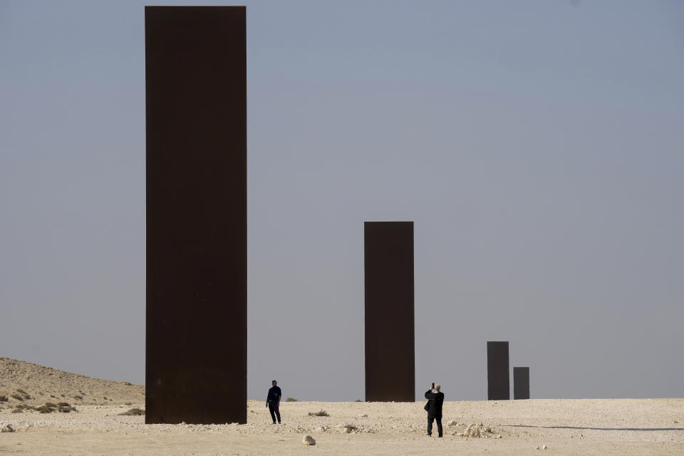 FILE - People view American artist Richard Serra's "East-West/West-East" art as it stands in a desolate section of the Brouq Nature Reserve in the northwestern part of the country's desert close to Zekreet, Qatar, Dec. 3, 2022. Serra, known for turning curving walls of rusting steel and other malleable materials into large-scale pieces of outdoor artwork that are now dotted across the world, died Tuesday, March 26, 2024, at his home in Long Island, N.Y. He was 85. (Nathan Denette/The Canadian Press via AP, File)