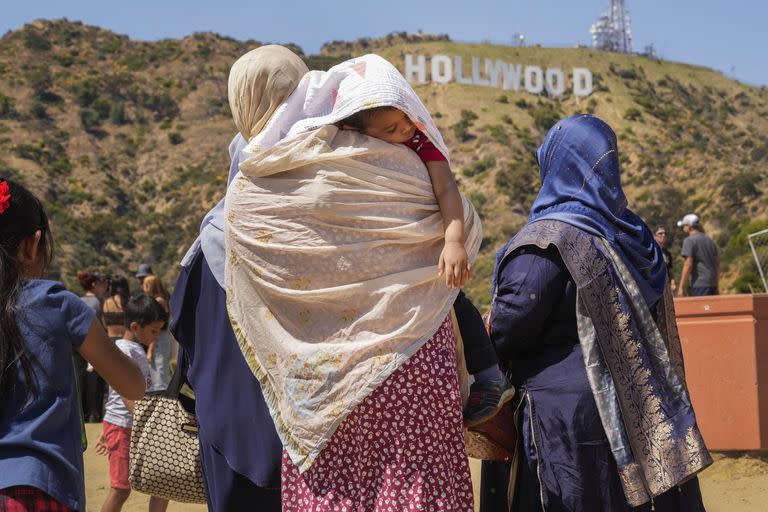 Turistas protegen a un niño dormido del sol mientras visitan el símbolo de Hollywood en Los Ángeles, el miércoles 12 de julio de 2023.