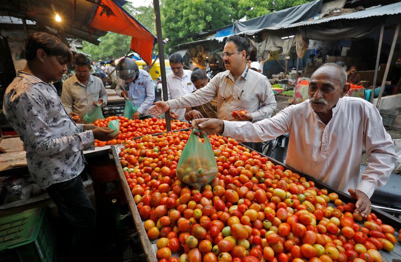 People buy tomatoes from a vendor at a vegetable market in Ahmedabad
