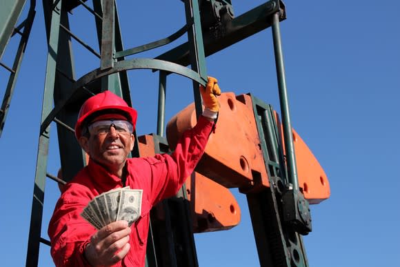 An oil worker on a pump handing out cash.