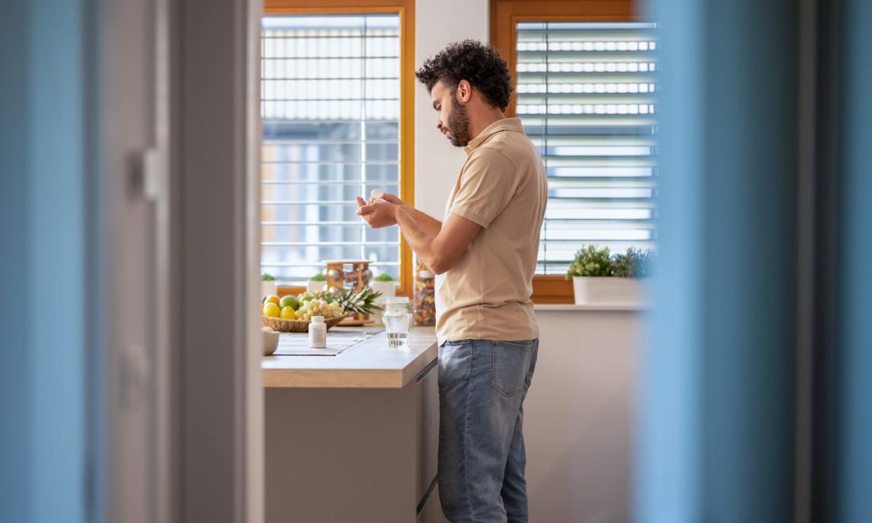 young man taking medicine with water at home