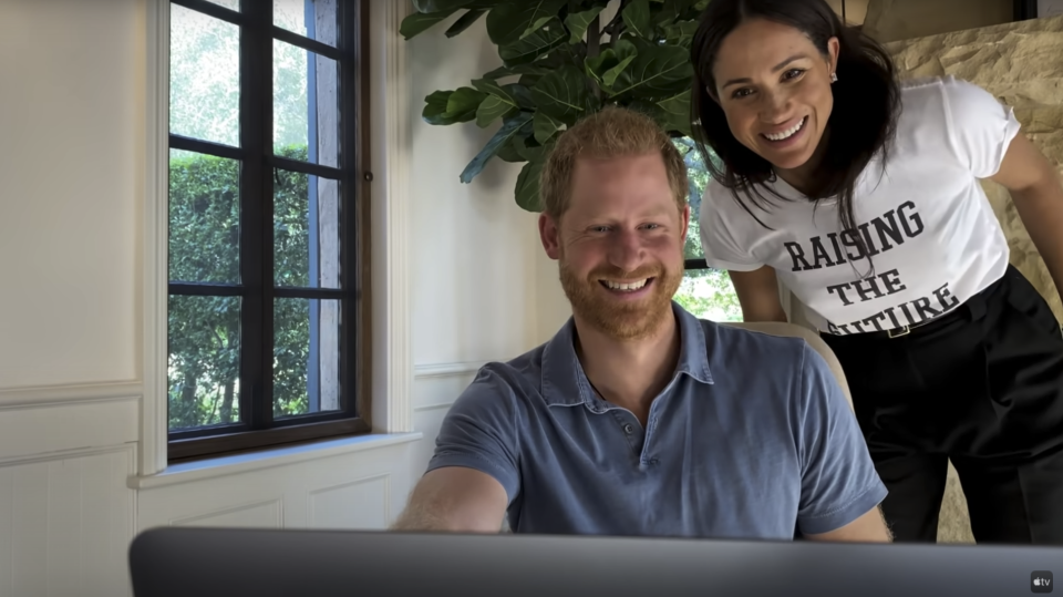 Harry's wife Meghan Markle is seen leaning over Harry while wearing a T-shirt