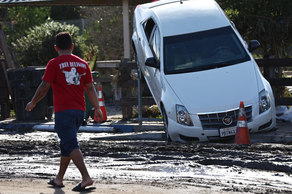 A person stands near a vehicle moved by flooding that remains lodged on a fence the day after an explosive rainstorm deluged areas of San Diego County on Jan. 23, 2024 in San Diego.