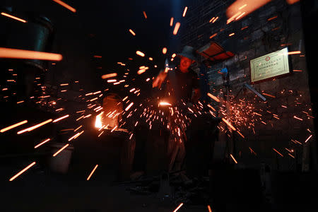 A blacksmith demonstrates hammering an iron piece at a workshop for handmade woks in Datian village, Hubei province, China August 13, 2018. REUTERS/Thomas Suen