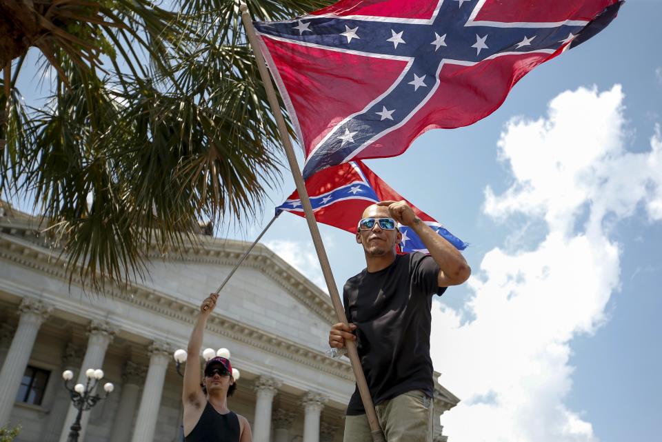 Otro de los símbolos más relevantes para el KKK es la bandera confederada, ya que en su mayoría defienden los valores de los antiguos secesionistas esclavistas. Dos partidarios ondean la divisa de la cruz azul durante una manifestación en Carolina del Sur.<br><br>Crédito: REUTERS/Chris Keane