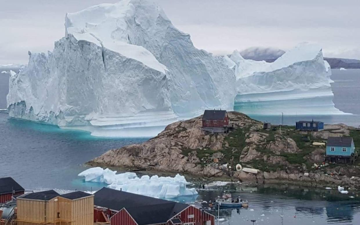 A giant iceberg is seen behind an Innaarsuit settlement, Greenland July 12  - REUTERS