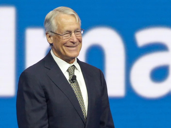 Rob Walton smiles while standing onstage in front of Walmart logo at shareholder meeting