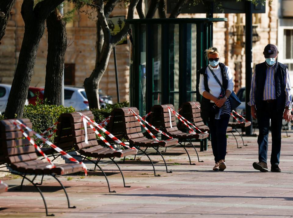 FILE PHOTO: A man and a woman wearing protective face masks walk past benches that have been taped off to prevent people from sitting on them, as people take advantage of the good weather to go outdoors in Sliema, despite the outbreak of the coronavirus disease (COVID-19) in Malta April 12, 2020. REUTERS/Darrin Zammit Lupi