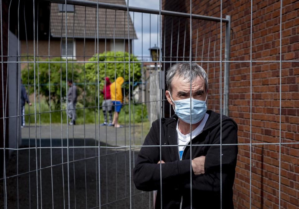 FILE - In this Tuesday, May 12, 2020 file photo, Iulian, Romanian worker who stands behind the fence that was set up at the entrance of a housing of Romania slaughterhouse workers in Rosendahl, Germany. Hundreds of the workers were tested positive on the coronavirus and were put on quarantine.More than 50,000 people have died after contracting COVID-19 in Germany, a number that has risen swiftly over recent weeks as the country has struggled to bring down infection figures. (AP Photo/Michael Probst, file)