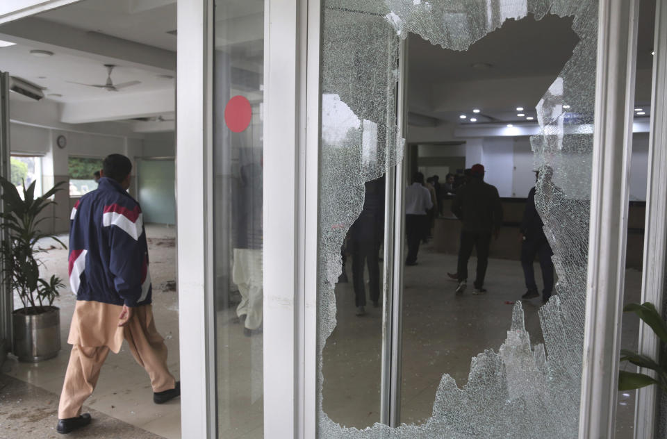 People walk next to broken window of hospital shattered by angry lawyers during a clash in Lahore, Pakistan, Wednesday, Dec. 11, 2019. Hundreds of Pakistani lawyers, angered over alleged misbehavior of some doctors toward one of their colleagues last month, stormed a cardiology hospital in the eastern city of Lahore, setting off scuffles with the facility's staff and guards that left heart patients unattended for several hours. (AP Photo/K.M. Chaudary)