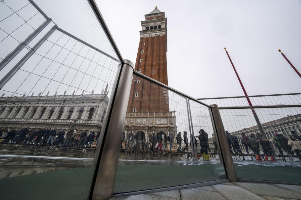 Tourists and residents walk on catwalks during a sea tide of around 97 centimeters (38.18 inches) to cross a flooded St. Mark's Square in Venice, northern Italy, Saturday, Dec. 10, 2022, where recently installed glass barriers prevent seawater from flooding the 900-year-old iconic St Mark's Basilica. St. Mark's Square is the lowest-laying city area and frequently ends up underwater during extreme weather. (AP Photo/Domenico Stinellis)