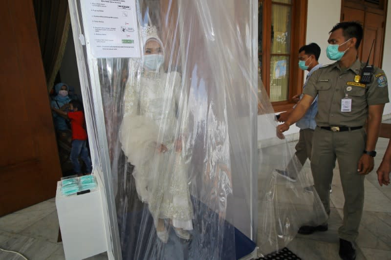 An Indonesian bride wearing a face mask is sprayed inside a disinfection chamber on her wedding day in Surabaya