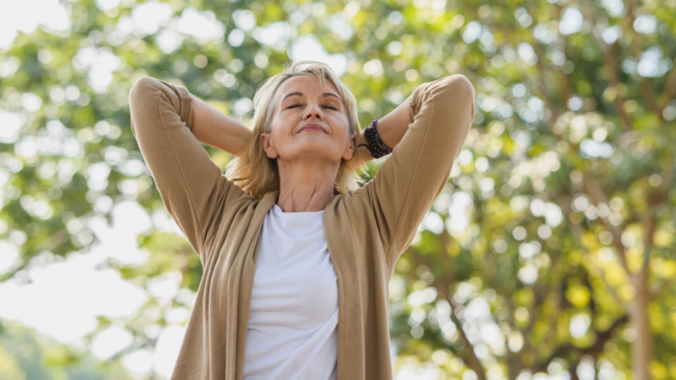 A woman with her hands behind her head standing a park to reduce cortisol