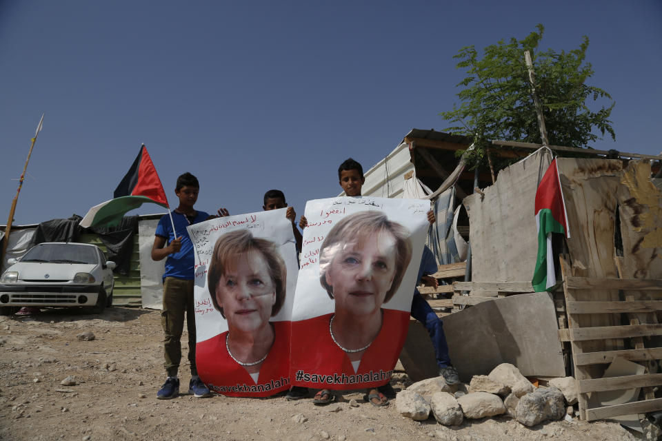 Bedouin children hold pictures of German Chancellor Angela Merkel ahead of her expected visit to Israel on Wednesday, in the West Bank Bedouin community of Khan al-Ahmar, Tuesday, Oct. 2, 2018. The children are pleading with Merkel to pressure Israel to halt demolition plans for the encampment of corrugated shacks outside an Israeli settlement east of Jerusalem. Arabic on the poster reads, "save Khan al-Ahmar" and "save our school." (AP Photo/Nasser Shiyoukhi)