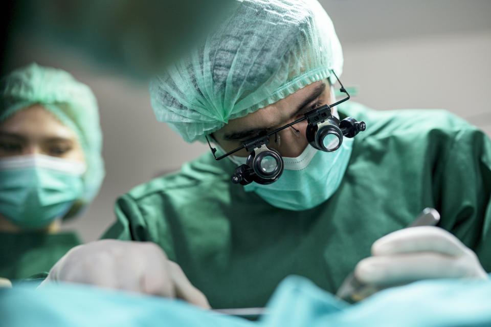 Two surgeons in the operating room wearing green scrubs, surgical masks and magnifying glasses performing a procedure