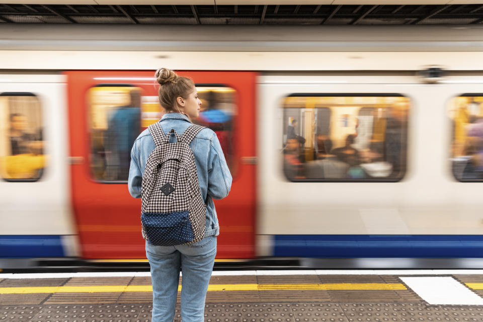 Rear view of young woman at subway station with incoming train