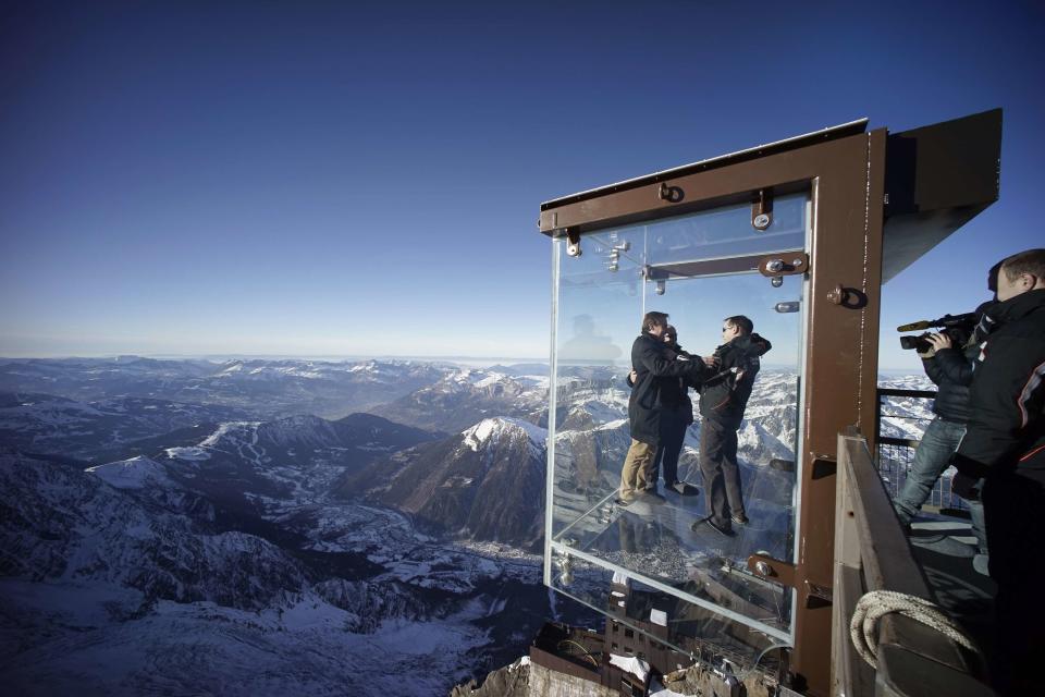 Journalists and employees, wearing slippers to protect the glass floor, stand in the 'Step into the Void' installation during a press visit at the Aiguille du Midi mountain peak above Chamonix, in the French Alps, December 17, 2013. The Chamonix Skywalk is a five-sided glass structure installed on the top terrace of the Aiguille du Midi (3842m), with a 1,000 metre drop below, where visitors can step out from the terrace, giving the visitors the impression of standing in the void. The glass room will open to the public on December 21, 2013. REUTERS/Robert Pratta (FRANCE - Tags: SOCIETY TRAVEL CITYSCAPE)