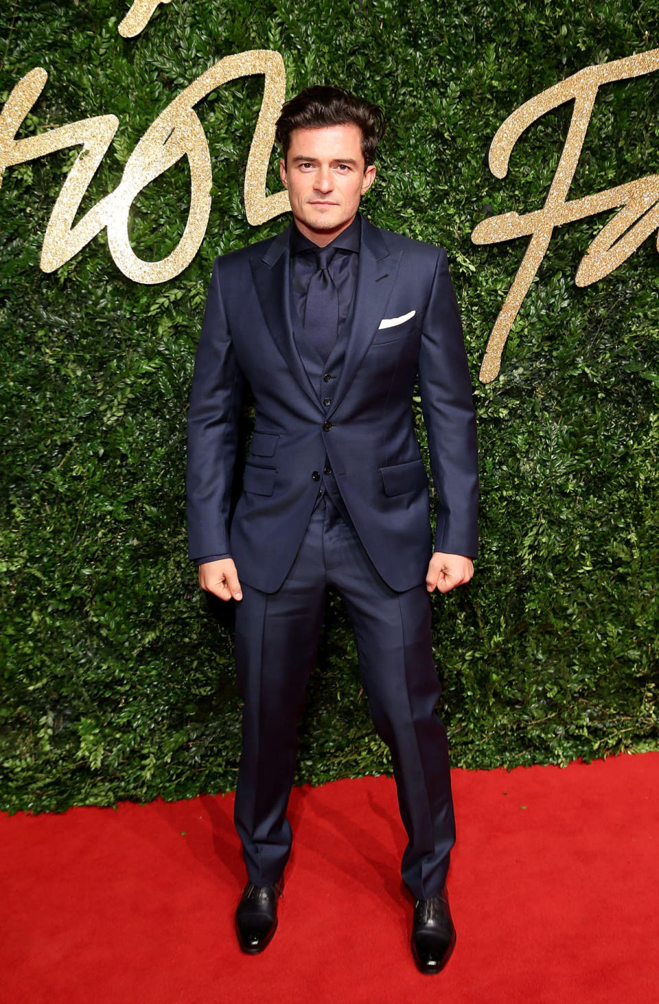 Orlando Bloom in a navy three-piece suit with matching shirt and tie.