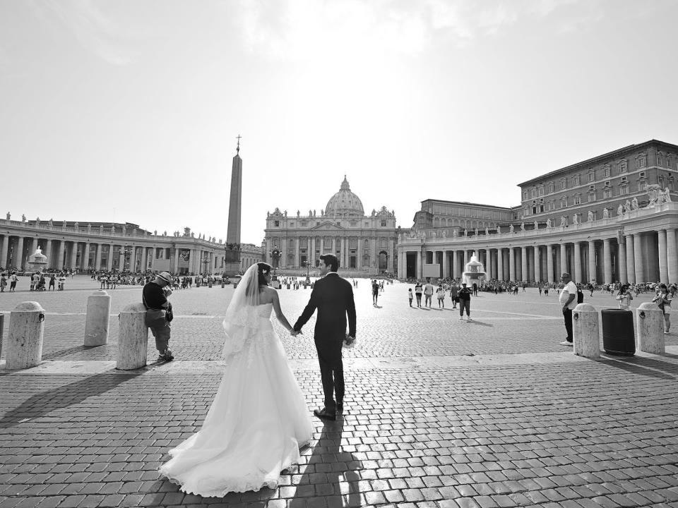 A bride and groom hold hands as they walk through a cobblestone street in Rome, Italy.