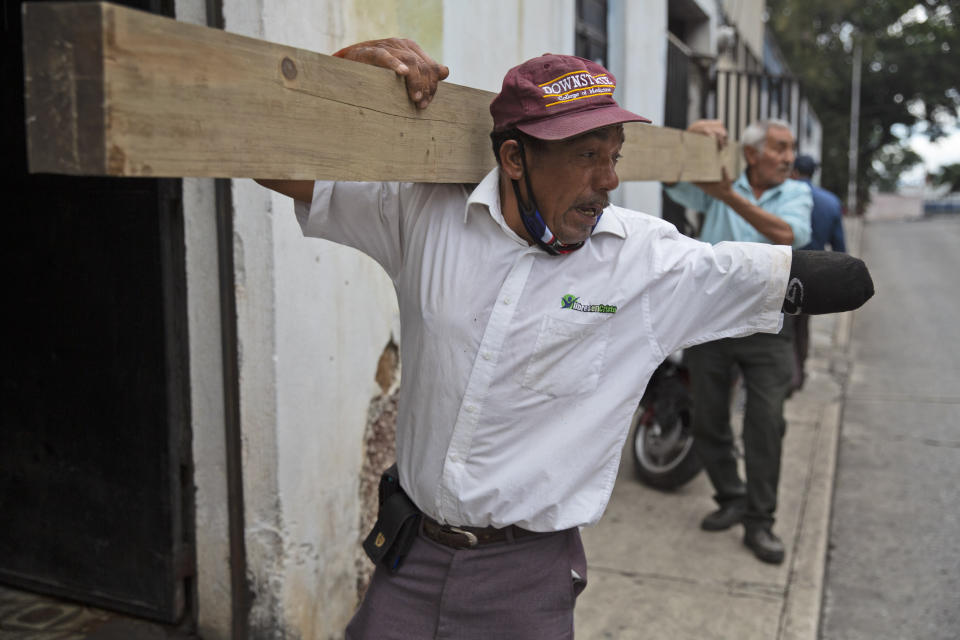 Los vendedores de helados Bernardo Pineda, de frente, y Alfredo Jiménez llevan una viga de madera que se usará para remodelar la casa en desuso utilizada para almacenar los carros de helados y donde viven algunos de los vendedores durante la pandemia de COVID-19 en la Ciudad de Guatemala, el viernes 29 de mayo de 2020. (AP Foto/Moises Castillo)