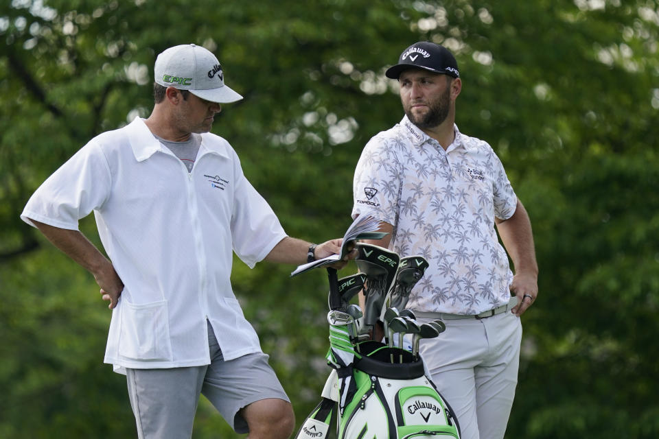 Jon Rahm talks with his caddie as he waits to hit on the 14th tee during the third round of the Memorial golf tournament, Saturday, June 5, 2021, in Dublin, Ohio. Rahm was later notified he tested positive for the coronavirus, knocking him out of the tournament. (AP Photo/Darron Cummings)