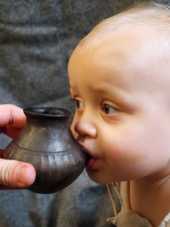 A baby is shown feeding from a reconstructed infant feeding vessel of the type investigated in research detailing prehistoric ceramic vessels