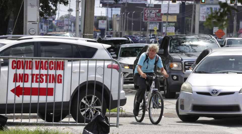 A cyclist passes cars at a standstill along West Colonial Drive in Orlando, Fla., Thursday, July 29, 2021, as residents wait in line for COVID-19 testing at Barnett Park. The line stretched through the park for more than a mile to the entrance to the Central Florida Fairgrounds. Orange County is under a state of emergency as coronavirus infections skyrocket in Central Florida. The Barnett Park site is testing 1,000 people a day and has closed early in recent days due to reaching capacity. (Joe Burbank/Orlando Sentinel via AP)