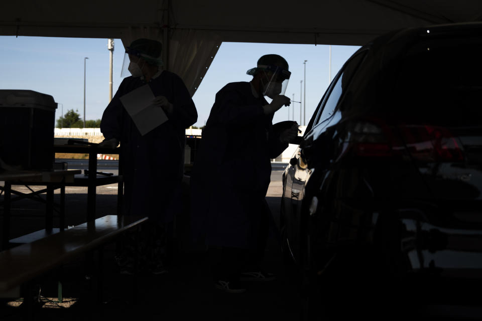 A member of medical personnel, wearing a full protective equipment, takes a mouth swab sample from a driver to be tested for coronavirus COVID-19 in a drive-in station in Luxembourg, Wednesday, May 27, 2020. Luxembourg has launch on Wednesday a nation wide coronavirus testing campaign among its population and commuters. (AP Photo/Francisco Seco)