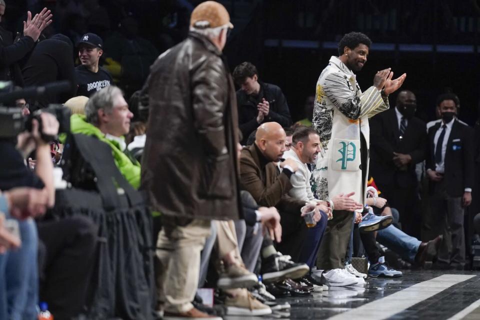 Kyrie Irving claps for his Nets teammates while standing by his front-row seat.