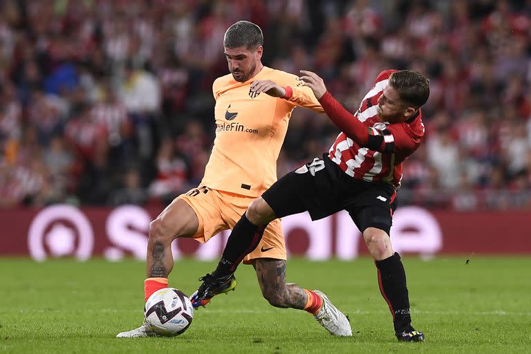 Rodrigo de Paul, de regreso a la titularidad tras casi un mes, forcejea con Muniain por la pelota, en el 1-0 de Atlético de Madrid como visitante de Bilbao por la liga de España.