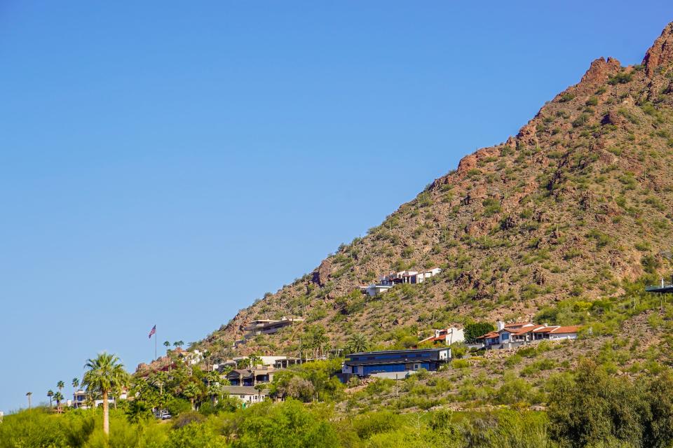 Mansion on the side of a red mountain dotted with cacti. Blue, clear skies in the background