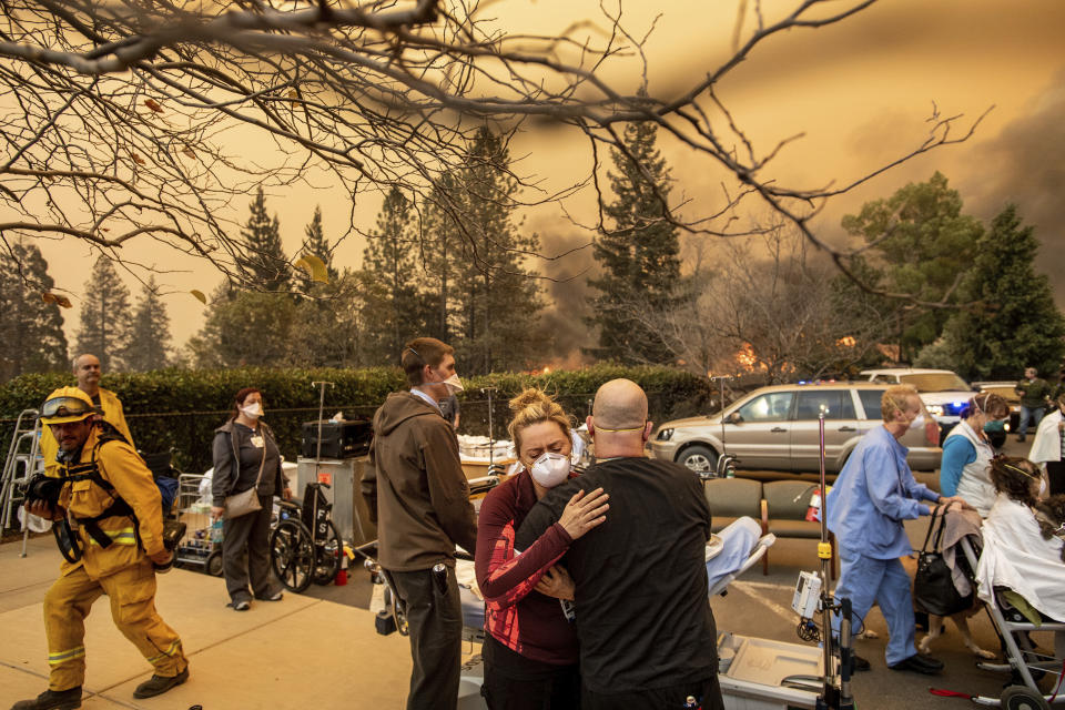 FILE - This Nov. 8, 2018, file photo shows Nurse Cassie Lerossignol hugs as coworker as the Feather River Hospital burns while the Camp Fire rages through Paradise, Calif. The scale of disaster in the Camp Fire was unprecedented, but the scene of people fleeing wildfire was familiar, repeated numerous times over the past three years up and down California from Redding and Paradise to Santa Rosa, Ventura and Malibu. In many of those communities, motorists became stuck in traffic as officials tried to evacuate thousands onto a few roads leading away from the flames. (AP Photo/Noah Berger, File)