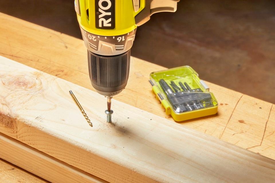 A person using a stripped screw extractor and a cordless drill/driver to remove a stripped screw in a wood stud..