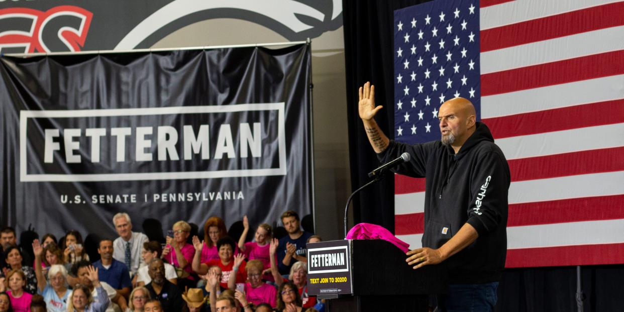 Fetterman with right hand raised in front of giant American flag