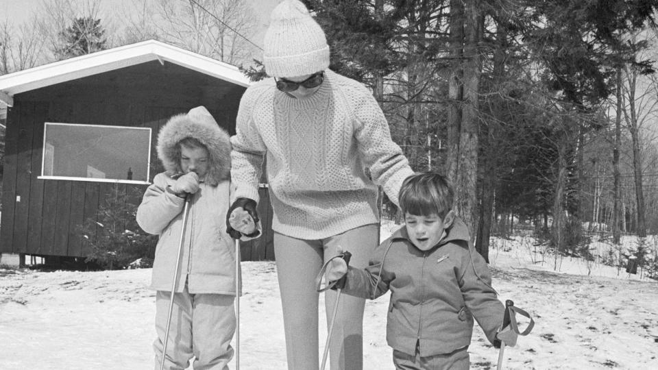 Jackie Kennedy, widow of the late President John F. Kennedy, stands with her children, Caroline and John, Jr., as they try out their skis on Mount Mansfield. The Kennedy clan has assembled here for Easter weekend.