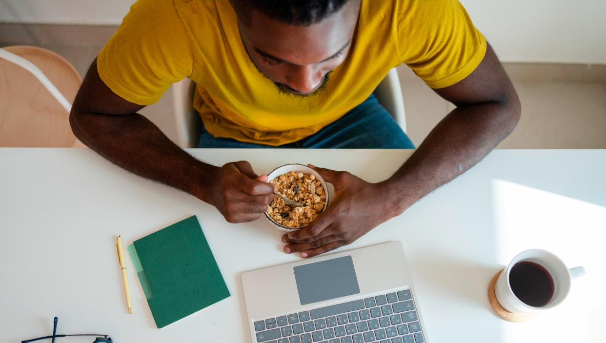  Man sitting in front of a laptop eating cereal. 