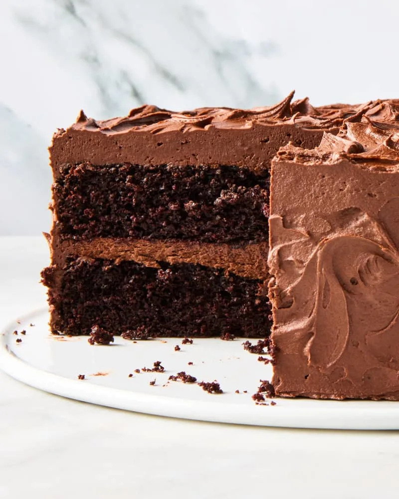 head on shot of a whole chocolate cake with icing, and a large slice taken out from it on the left.