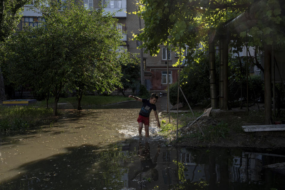 A boy plays in a back yard in Kherson, Ukraine, Tuesday, Jun 6, 2023 which was flooded after the Kakhovka dam was blown up overnight. The wall of a major dam in a part of southern Ukraine has collapsed, triggering floods, endangering Europe's largest nuclear power plant and threatening drinking water supplies. (AP Photo/Evgeniy Maloletka)