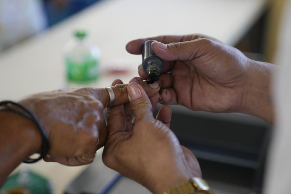 An election worker places ink on the fingers of a man after he has finished voting at a polling center Monday, May 9, 2022 in Quezon City, Philippines. Filipinos were voting for a new president Monday, with the son of an ousted dictator and a champion of reforms and human rights as top contenders in a tenuous moment in a deeply divided Asian democracy. (AP Photo/Aaron Favila)