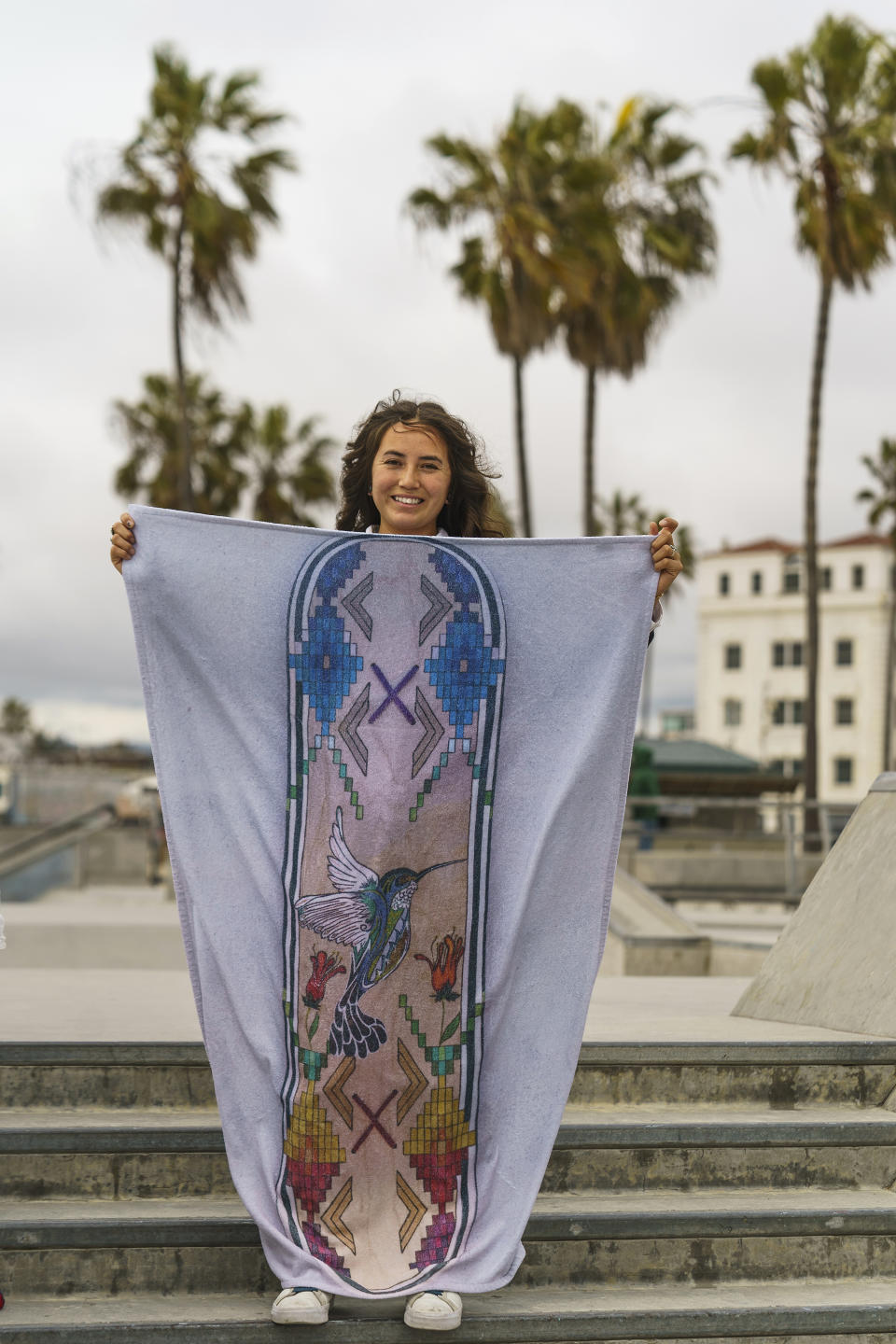 Di'Orr Greenwood, an artist born and raised in the Navajo Nation in Arizona and whose work is featured on the new U.S. stamps, holds a towel up with one of her skateboard designs in the Venice Beach neighborhood in Los Angeles Monday, March 20, 2023. On Friday, March 24, the U.S. Postal Service is debuting the "Art of the Skateboard," four stamps that will be the first to pay tribute to skateboarding. The stamps underscore how prevalent skateboarding has become, especially in Indian Country, where the demand for designated skate spots has only grown in recently. (AP Photo/Damian Dovarganes)