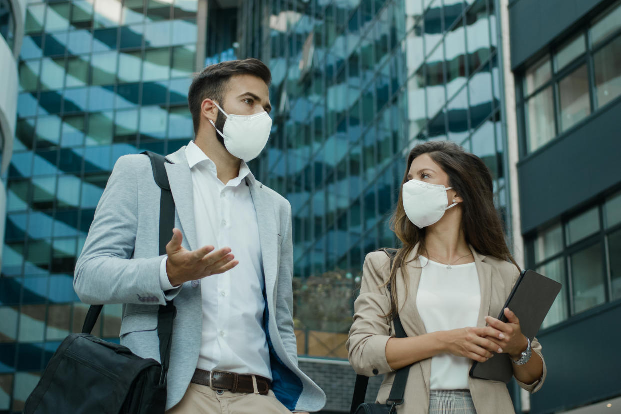 Two business people wearing protective face masks and talking to each outdoors